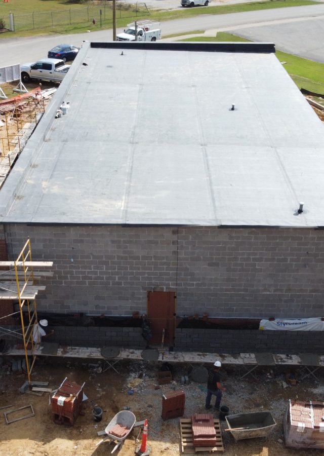 A drone shot of the exterior of the new Chester County 911 building under construction. Scaffoldings can be seen on the left side. Three construction workers wearing hard hats and another construction worker can be seen on the foreground. Three construction trucks are on the side of the road.